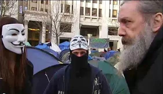 Alan Moore speaks with Occupy demonstrators wearing Guy Fawkes masks based on the titular character in V For Vendetta